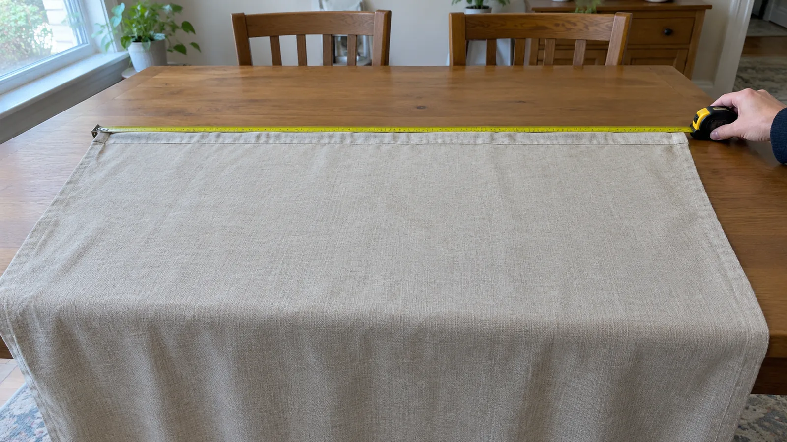 Flat curtain fabric spread across a dining table with a tape measure spanning its top edge