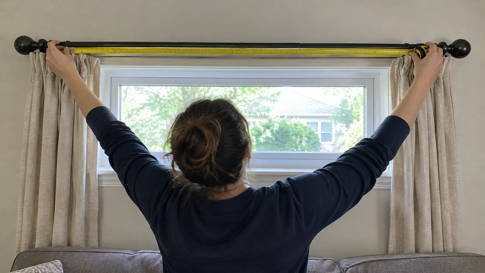 Resident measuring across a curtain rod above a window, with the decorative finials visible at either end