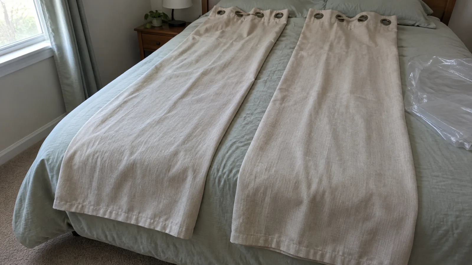 Two matching grommet curtain panels laid separately on a bed beside plain opened packaging