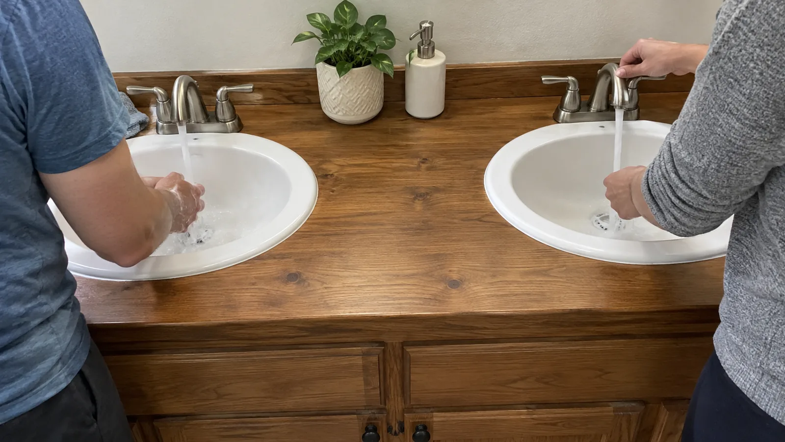 Two adults using the separate basins of a double vanity at the same time, with both basins and the counter between them visible