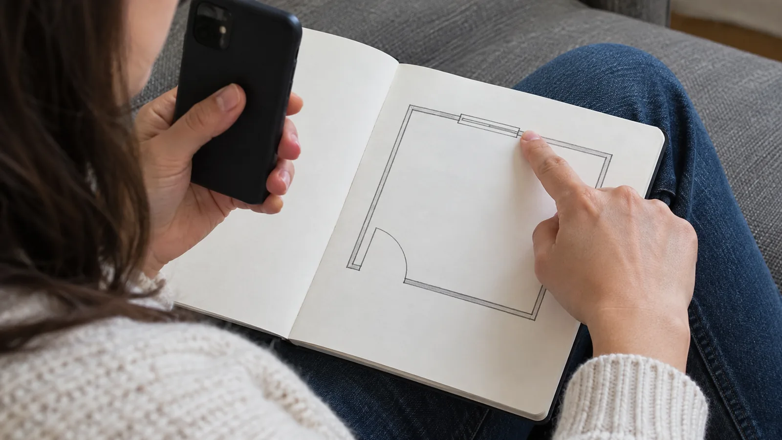 Person pointing to a window position on a room sketch while consulting a phone