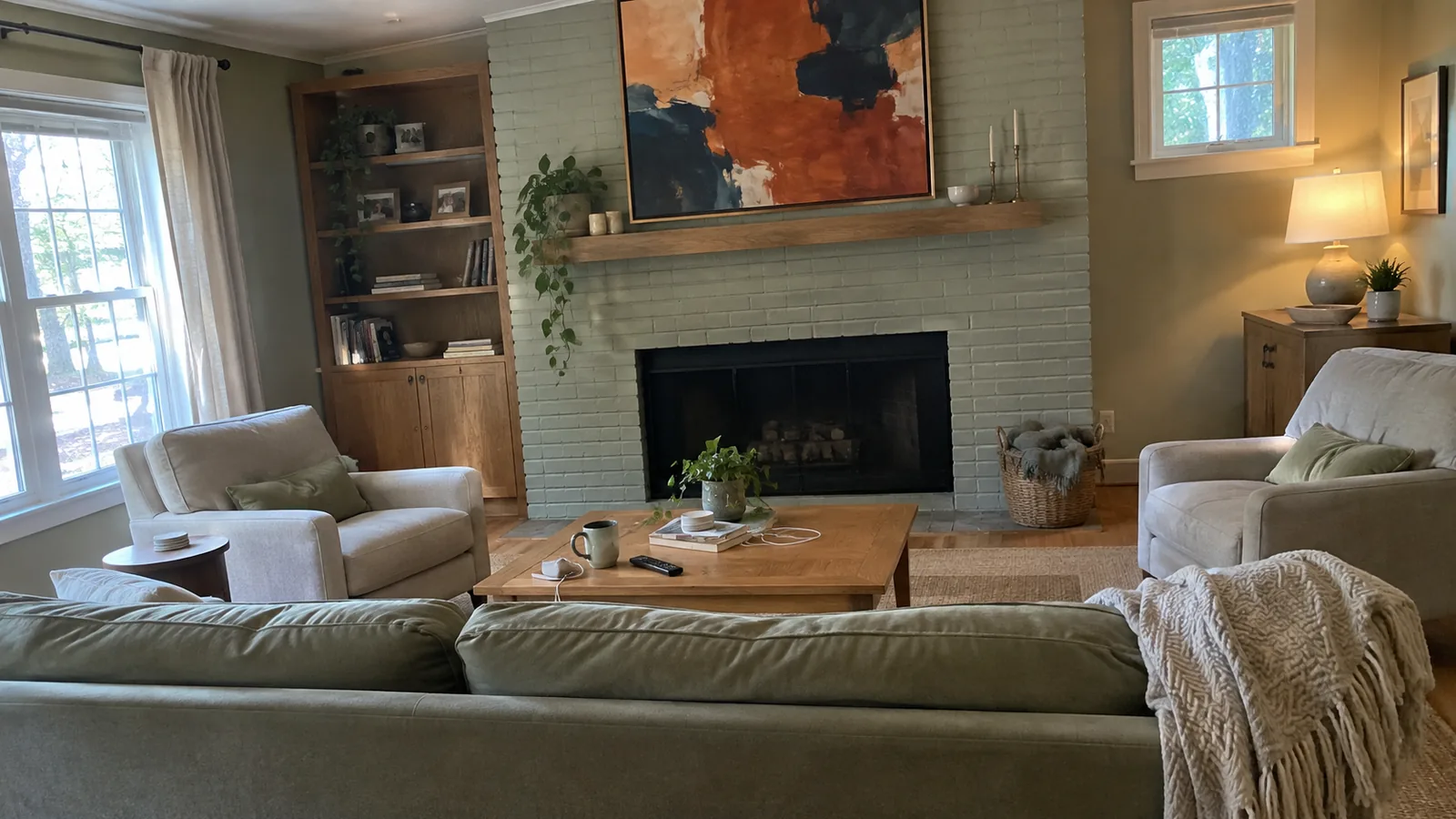 Living room where a sofa and two armchairs face a fireplace with a large abstract painting above the mantel, the only strong contrast in the room