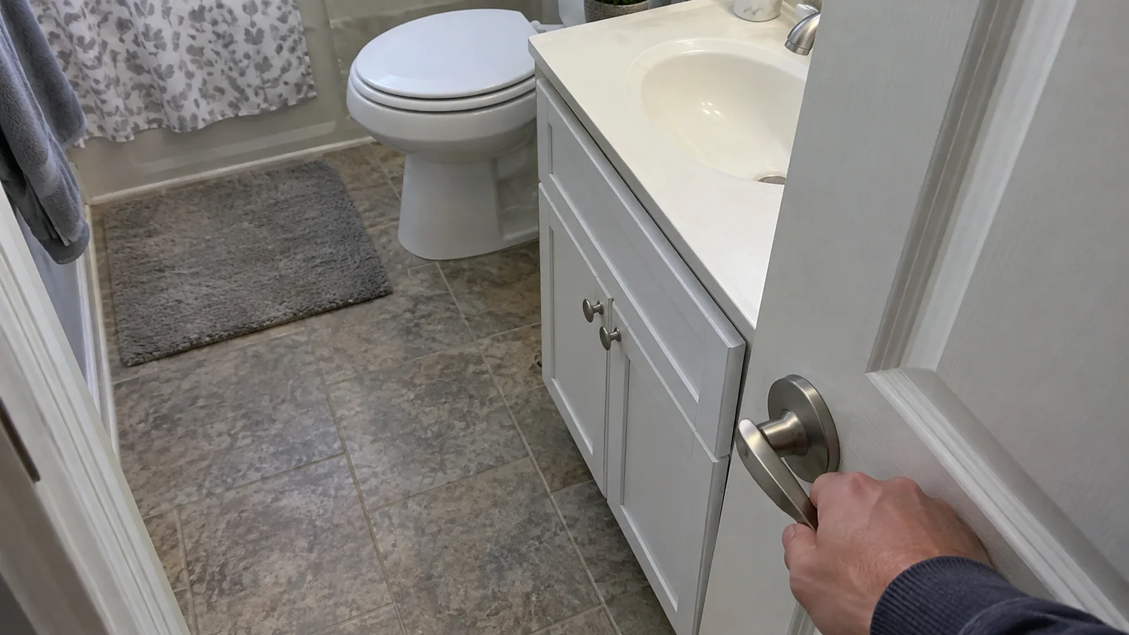 Bathroom door swung open into the room with its edge passing just in front of a shallow white vanity, seen from the doorway