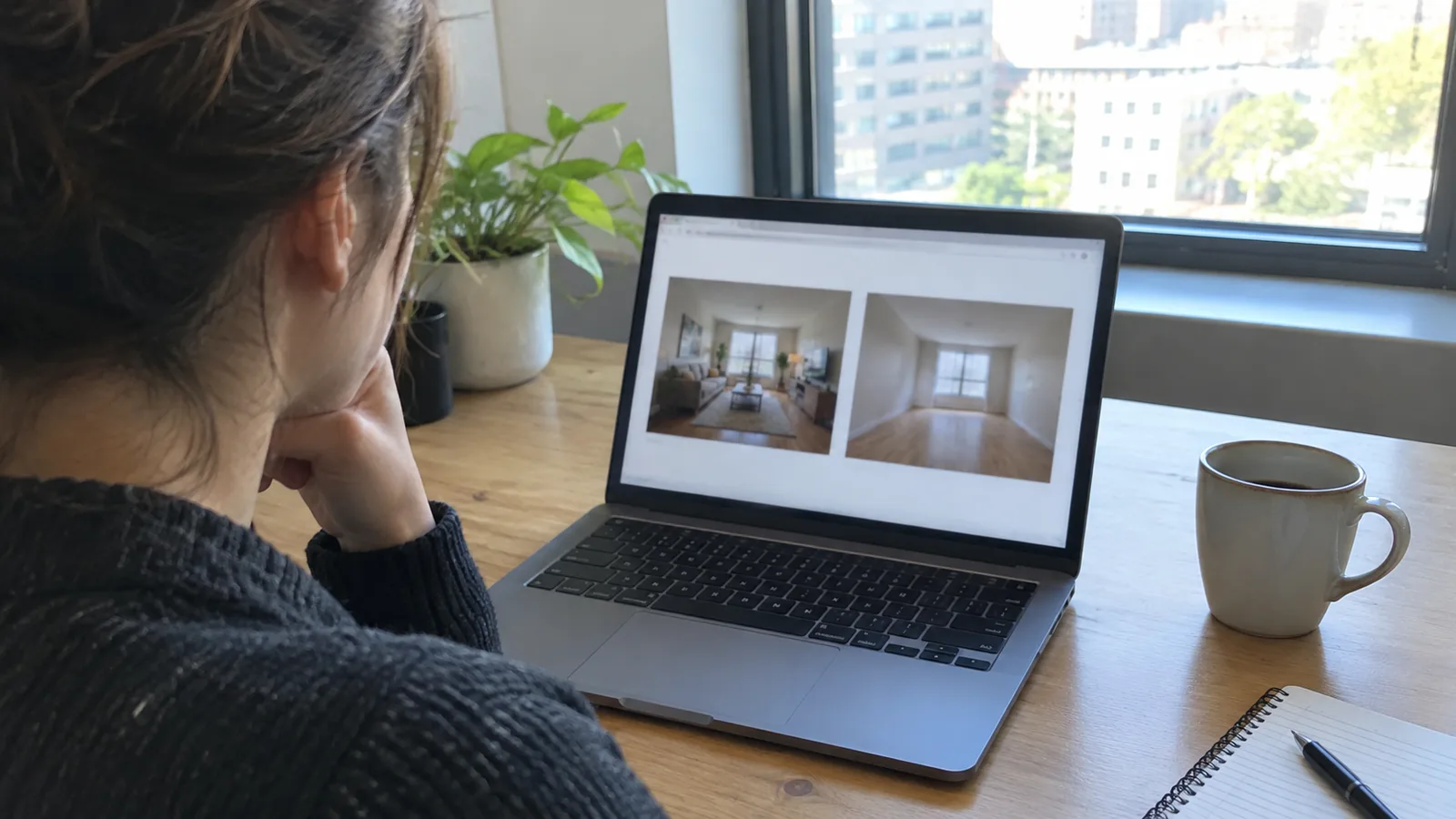 A real estate agent at a desk comparing a staged living room photo and the original empty room photo side by side on a laptop screen