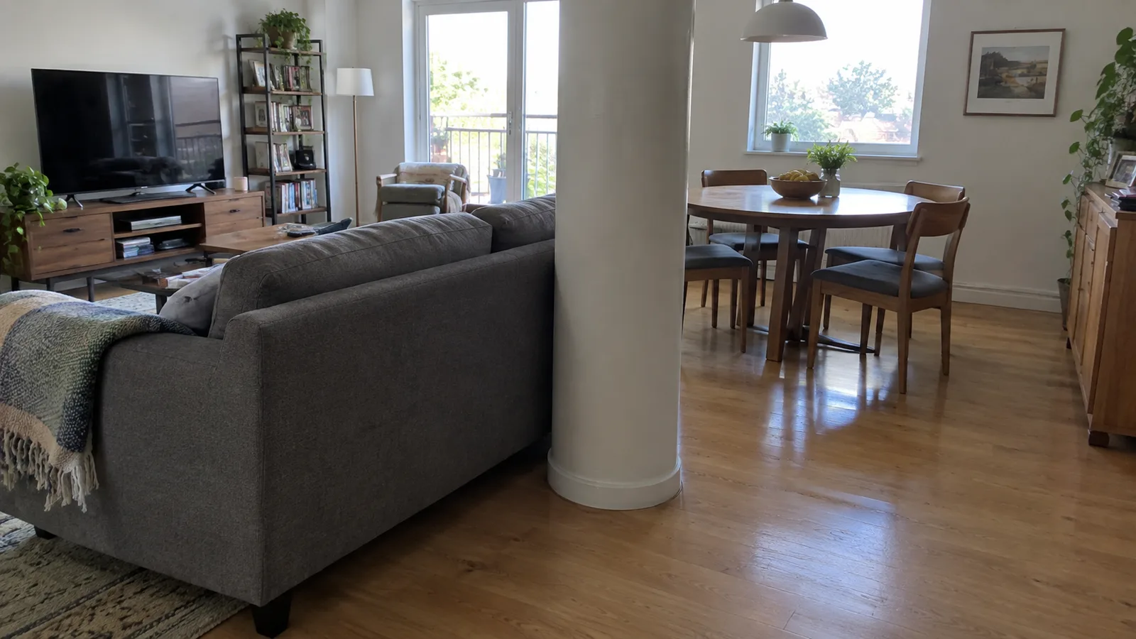 A living room with a round column near the middle, with the back of a sofa lined up beside it and a dining table visible beyond