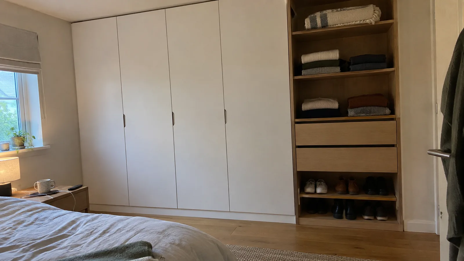Wall of white modular wardrobes with a mix of hinged doors and an open section with shelves and drawers in a calm bedroom